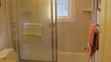 Une salle de bain avec une douche à parois de verre, une baignoire, des toilettes et une fenêtre.