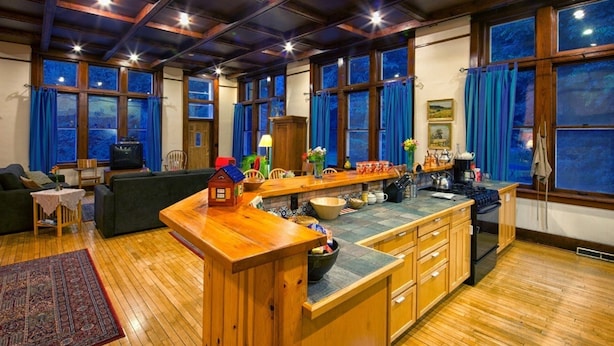 A cozy kitchen with wooden cabinets, a central island, and large windows with blue curtains.