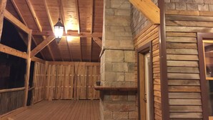 Una terraza de madera con un muro de piedra y una puerta, bajo un techo de madera con vigas.