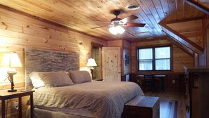 Un dormitorio acogedor tipo cabaña de madera, con cama, dos lámparas de noche, un ventilador de techo y una ventana.