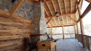 Un espacio interior con piso de madera, chimenea de piedra, mesa de fútbol de mesa y una lámpara colgante.