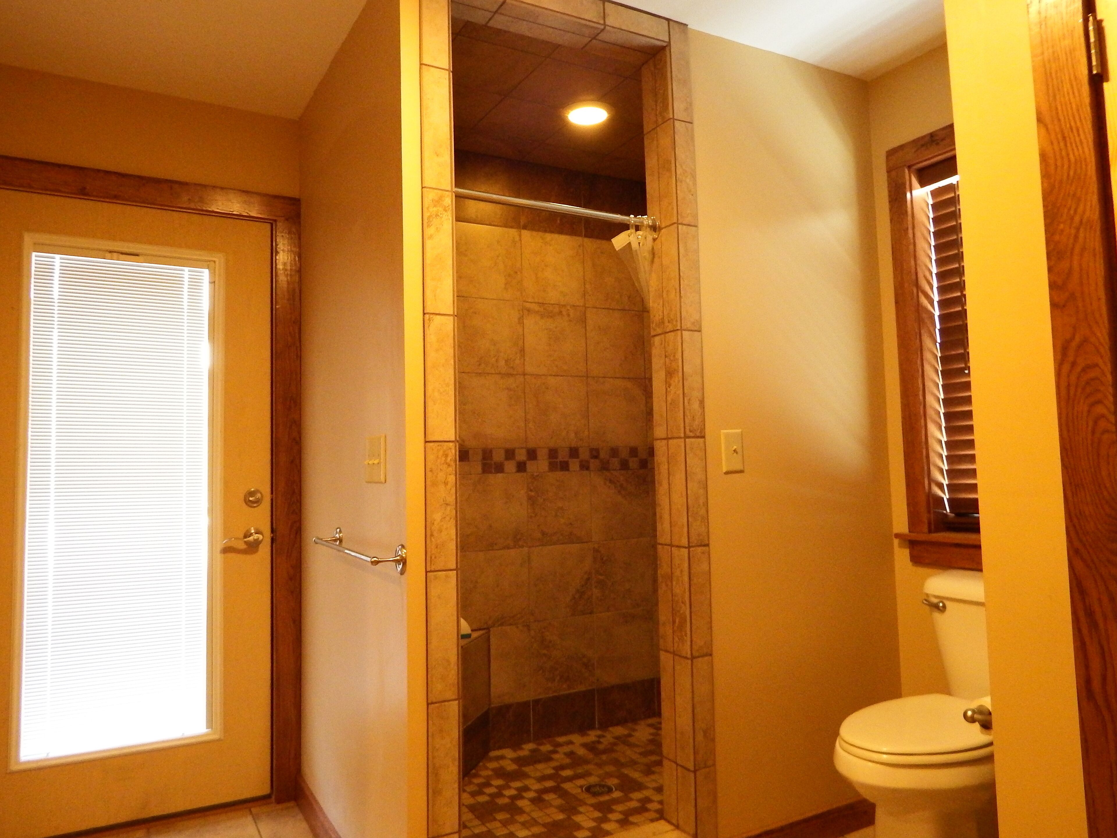 A bathroom with a shower, toilet, and a window with blinds.
