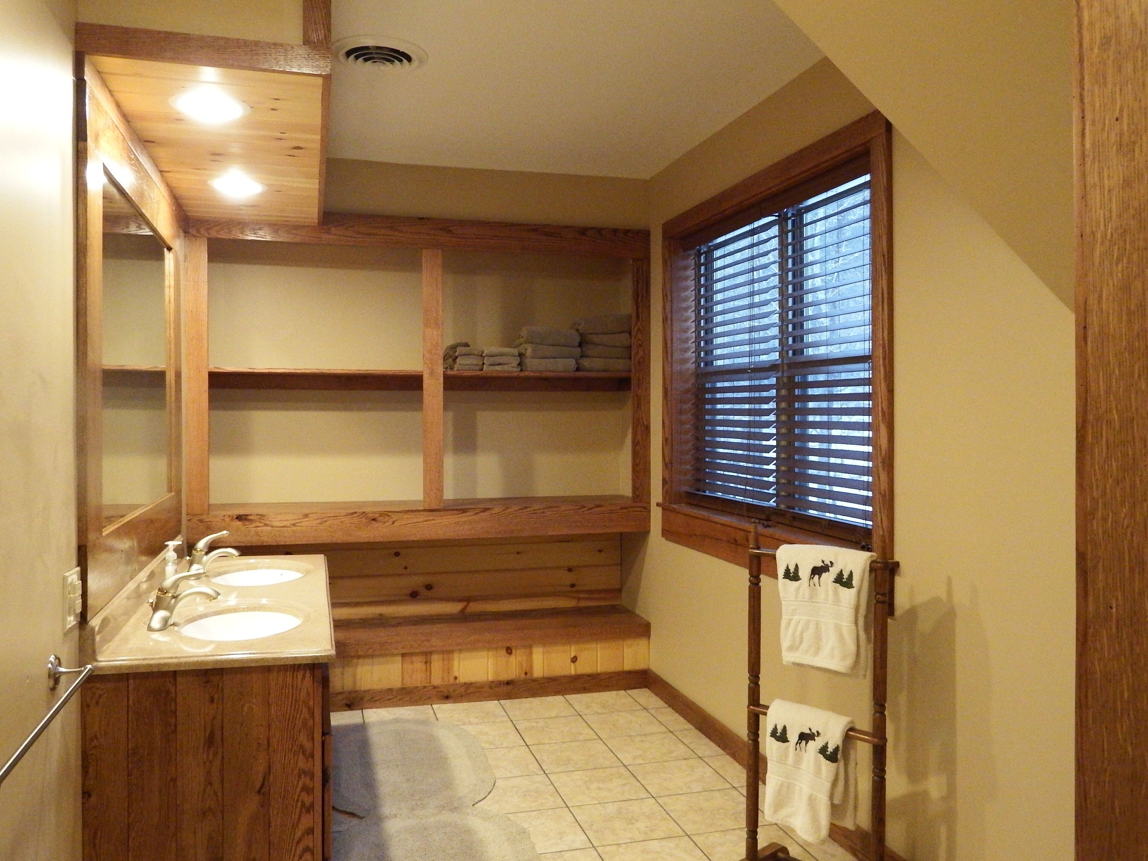 Un bagno con scaffali in legno, un doppio lavabo e una finestra con persiane.