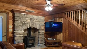 Una sala de estar acogedora con chimenea de piedra, sofás de cuero, un televisor y una escalera de madera.