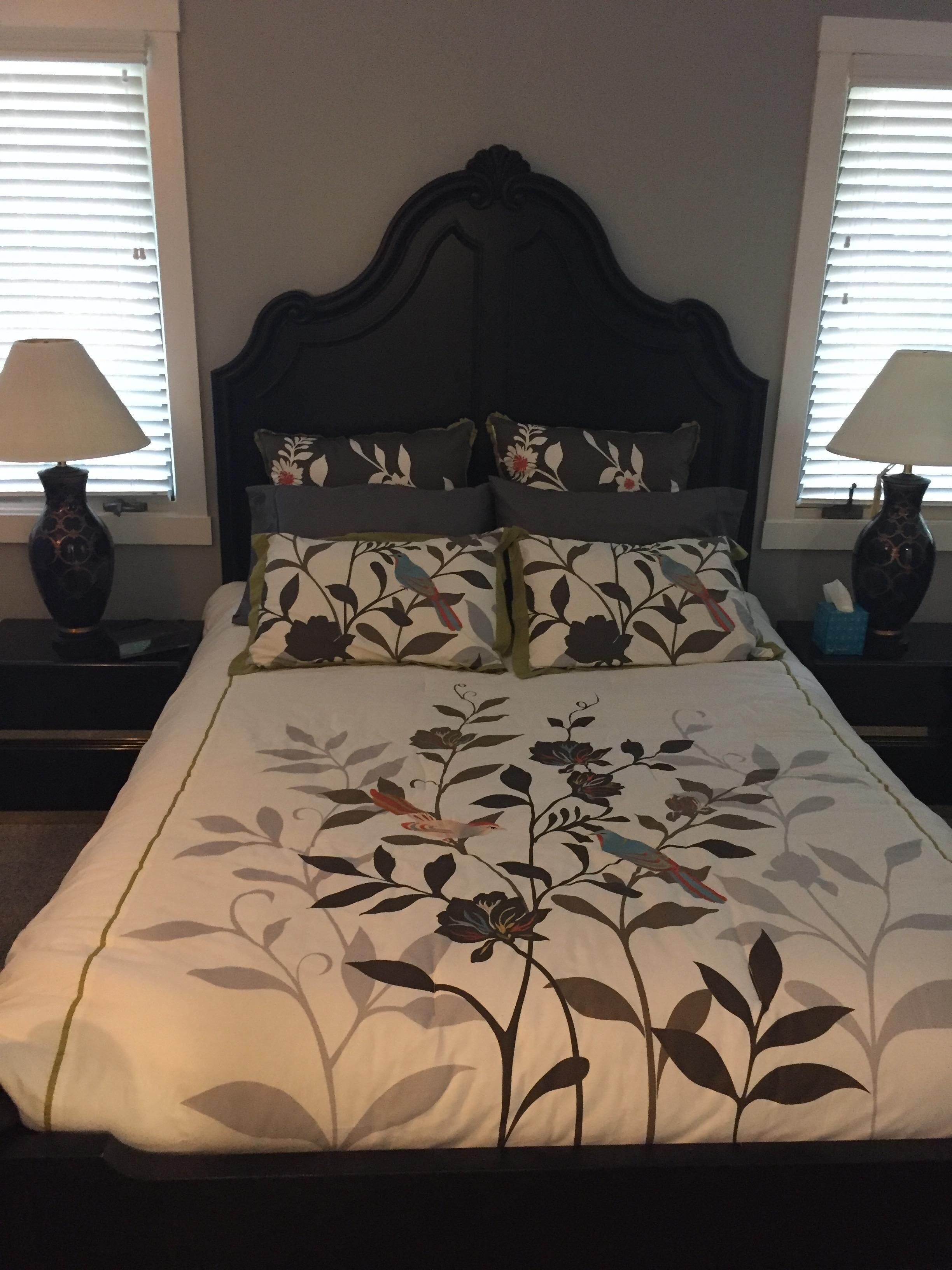 Een net opgemaakt bed met bloemenbeddengoed, omringd door twee nachtkastjes met lampen en decoratieve vazen.