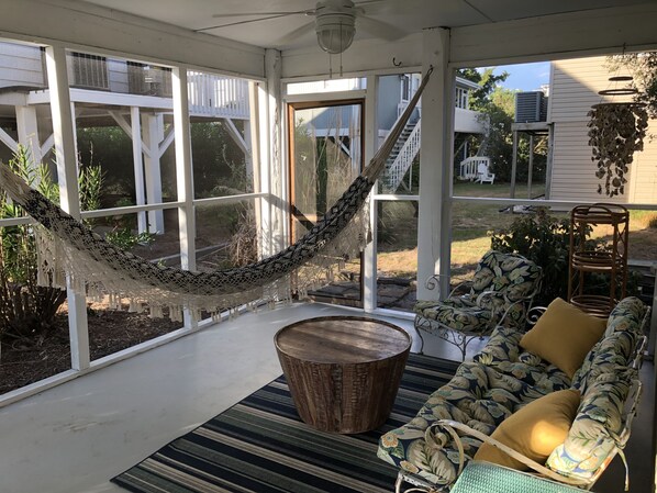 A covered porch with a hammock, a wooden coffee table, and a floral sofa.