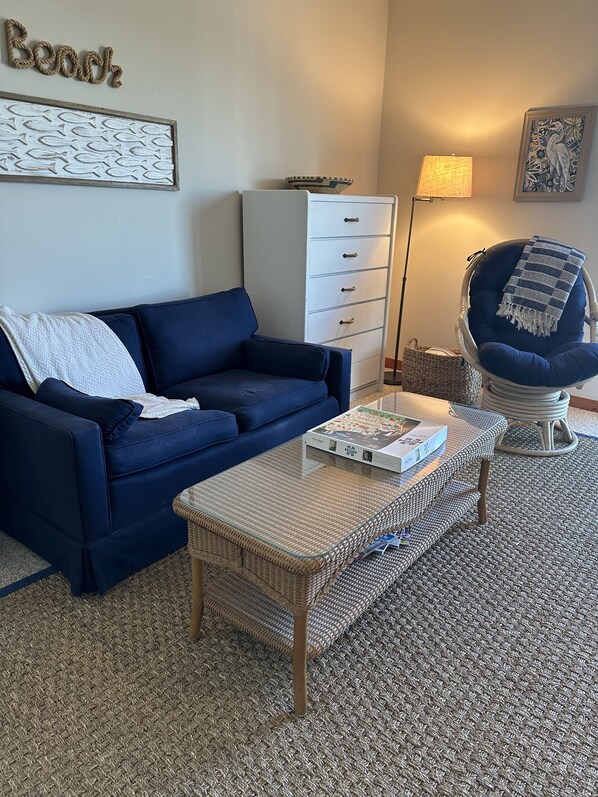 A living room with a blue sofa, a wicker coffee table, a white cabinet, a wicker chair, and a lamp. - Pelican Hub, a beach house in beautiful Sunset Beach, 1 block from beach access! (Sunset Beach)