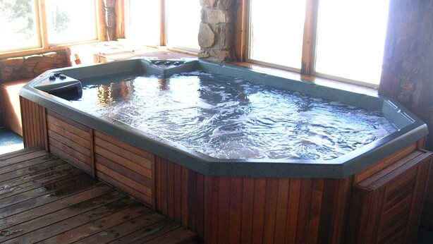 Un jacuzzi con cubierta de madera y paredes de piedra.