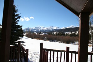 A view from a wooden porch with a snow-covered landscape and mountains in the background.