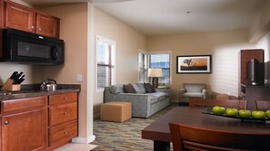 Cozy living space with a kitchenette, sofa, armchair, and artwork.