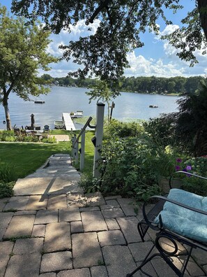 Un chemin de pierre mène à une terrasse au bord du lac, où se trouvent un banc et du mobilier d’extérieur.