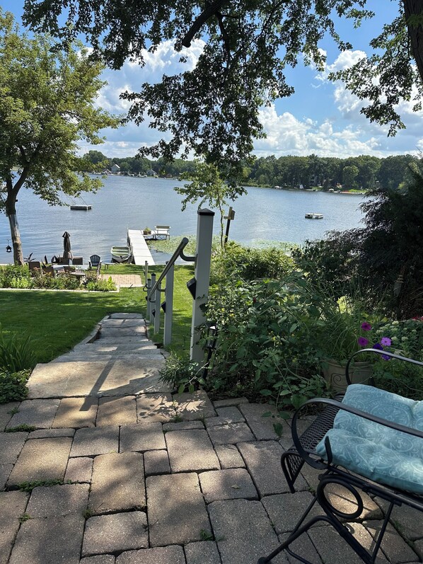 Un chemin de pierre mène à une terrasse au bord du lac, où se trouvent un banc et du mobilier d’extérieur.