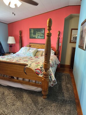 A bedroom with a wooden bed, floral bedding, a red wall, and a ceiling fan.