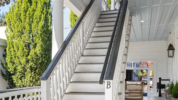 A white staircase with a black handrail leading to an upper level. - Southern Ease Contemporary Flair | The Charleston (Charleston)