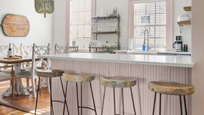 A kitchen with a wooden bar stool area, a white countertop, and hanging geometric light fixtures. - Southern Ease Contemporary Flair | The Charleston (Charleston)