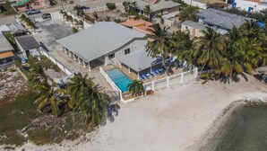 Vue aérienne d’une propriété située sur la côte, avec une piscine, des palmiers et une plage.