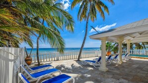 Une terrasse au bord de la plage, avec des chaises longues blanches et une clôture blanche.