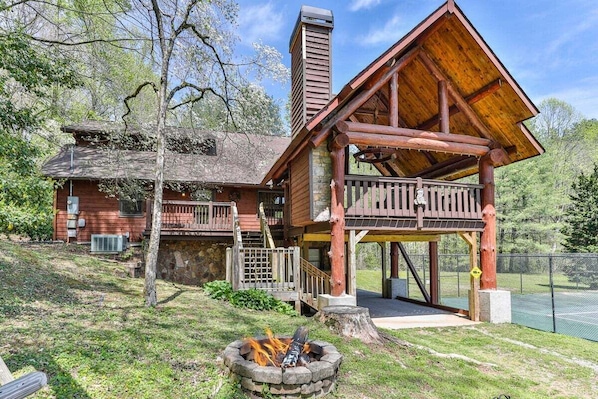 A rustic cabin with a wooden deck, a fire pit, and a stone chimney.