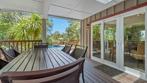 Et overdækket spiseområde med pool, træterrasse og glasdøre, der fører ud til en patio.
