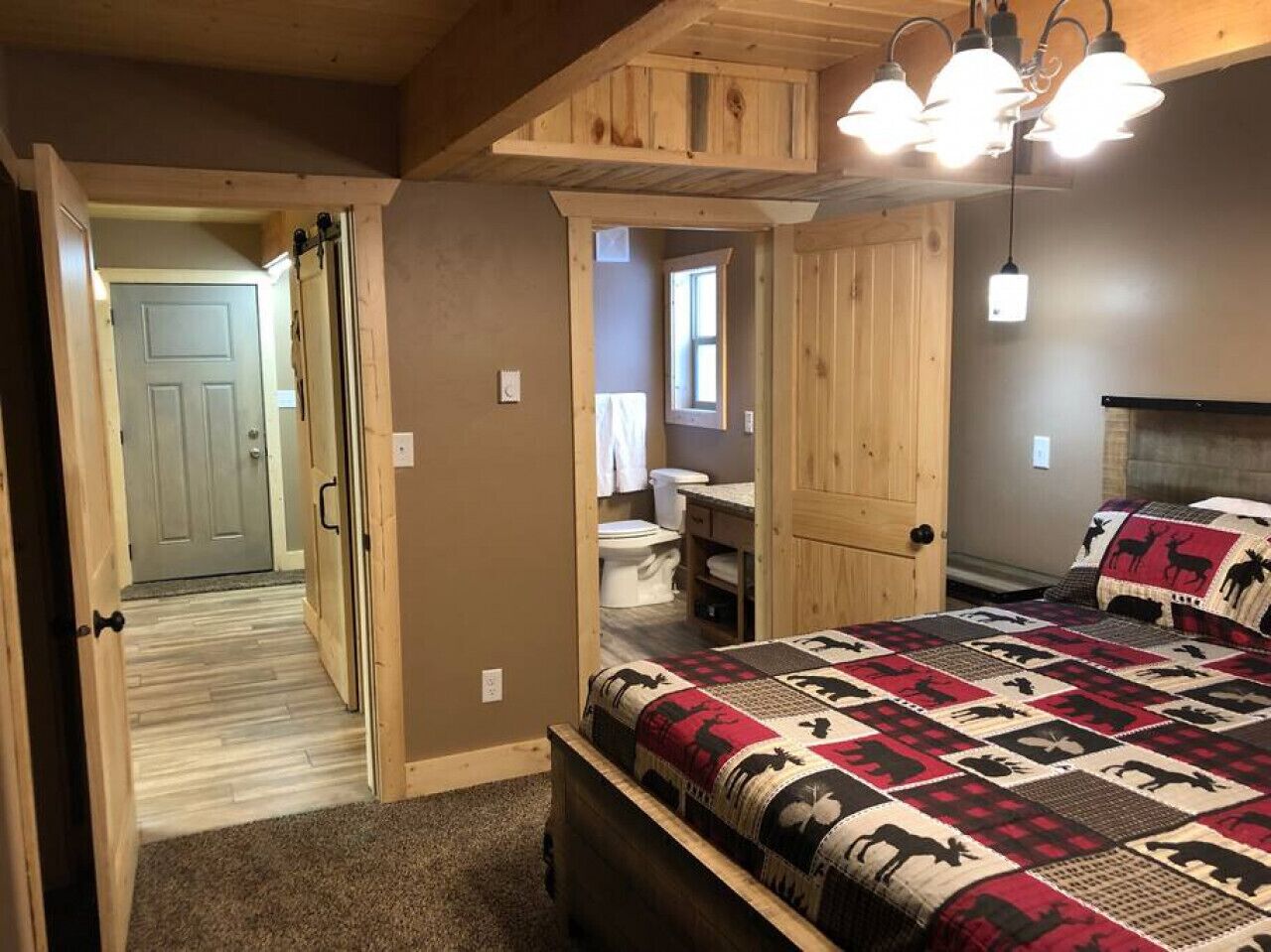 Una camera da letto con un letto, soffitto in legno e bagno visibile attraverso una porta aperta.