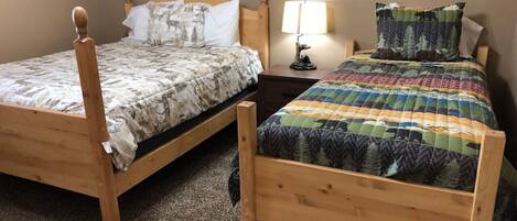 Dos camas de madera con ropa de cama diferente, una mesita de noche con lámpara y techo de madera.