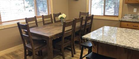 A kitchen with a wooden dining table, six chairs, a granite countertop, and a clock on the wall.