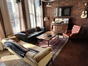 A cozy living room with a leather sofa, a brown armchair, a wooden coffee table, and a TV mounted on a brick wall.