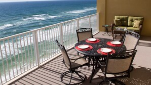 A balcony with a table set for four, overlooking the ocean.