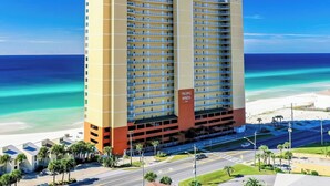 A high-rise hotel with multiple balconies, located near a beach with clear turquoise waters.