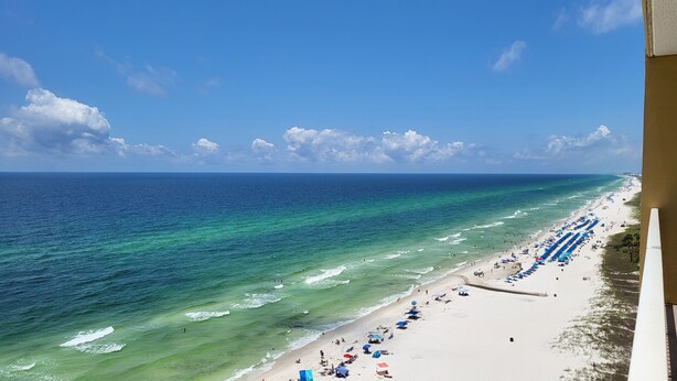 A beach with clear turquoise waters, a sandy shore, and a row of blue umbrellas.