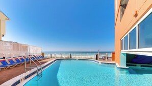 A pool area with clear blue water, sun loungers, and a view of the ocean.