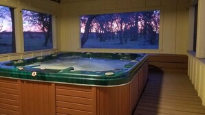 Een jacuzzi in een overdekte buitenruimte met ramen met uitzicht op een besneeuwd landschap.