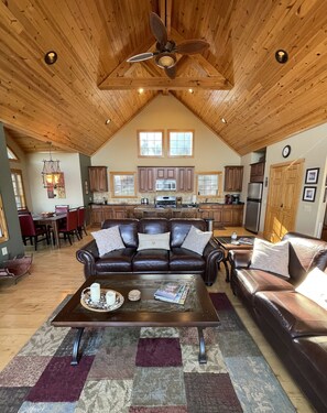 A spacious living room with a high ceiling, a ceiling fan, and a large window.