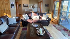 A spacious living room with leather sofas, a coffee table, and a large window offering a view of the outdoors.