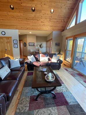 A spacious living room with leather sofas, a coffee table, and a large window offering a view of the outdoors.