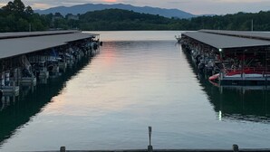 A calm river with boats docked on both sides, surrounded by greenery and mountains in the distance.