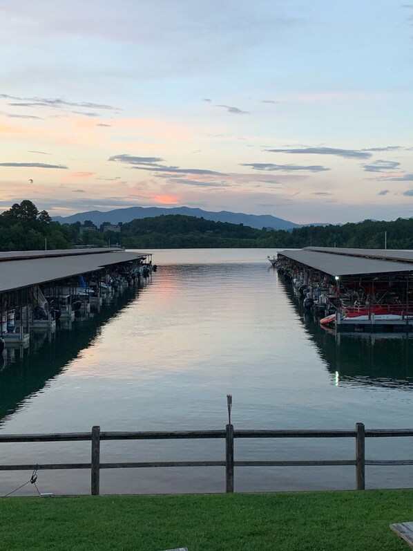 A calm river with boats docked on both sides, surrounded by greenery and mountains in the distance.