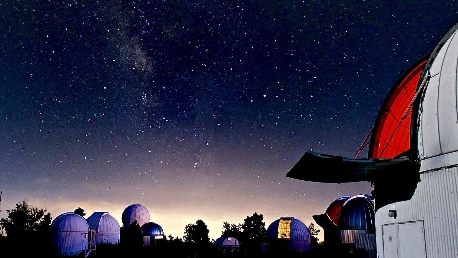 Cielo nocturno con estrellas y varias estructuras abovedadas, probablemente observatorios, bajo un cielo despejado.