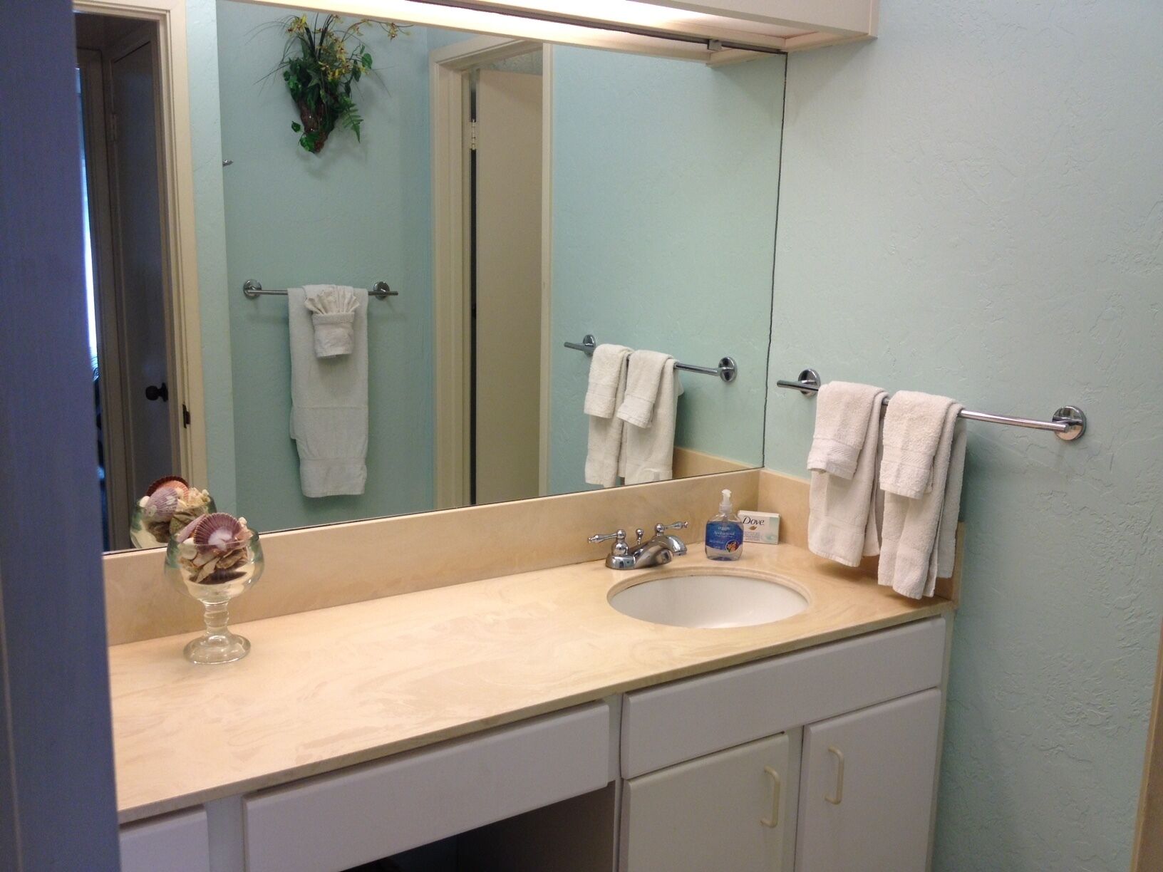 A bathroom with a sink, mirror, towel rack, and a glass vase with seashells.