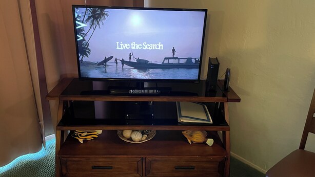 Ein Flachbildfernseher auf einer Holzunterhaltungseinrichtung, auf dem eine Strandansicht zu sehen ist.