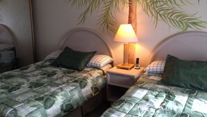 Ein Hotelzimmer mit zwei Betten, jedes mit einem Palmenblatt-Kopfstück und einer Lampe auf dem Nachttisch.