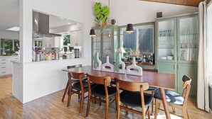 A modern kitchen with wooden cabinetry, a central island, and a dining area with wooden chairs. - Spacious 4BD Beach House - Pet-Friendly - Hot Tub! (Manzanita)