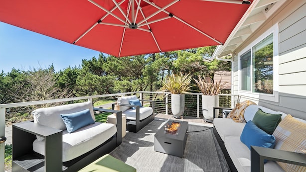 An outdoor patio with a red umbrella, a gray sofa, and a fire pit. - Spacious 4BD Beach House - Pet-Friendly - Hot Tub! (Manzanita)