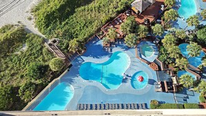 An aerial view of a resort with multiple swimming pools, lounge areas, and a beach area. - Oceanfront Condo just steps to the beach, Free parking and no resort fees! (North Myrtle Beach)