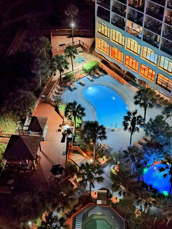 An aerial view of a hotel with a swimming pool, palm trees, and a building with multiple floors and balconies.