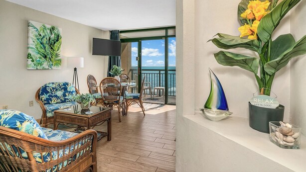 A living room with wicker furniture, a television, and a view of the sea. - Oceanfront Condo just steps to the beach, Free parking and no resort fees! (North Myrtle Beach)