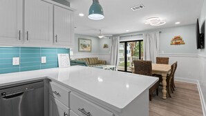 Une cuisine moderne avec des meubles blancs, un grand îlot central et un coin repas comprenant des chaises et une table en osier.