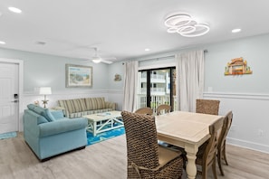 Un salon comprenant un canapé, une table à manger avec des chaises, un ventilateur de plafond et une fenêtre avec des rideaux.