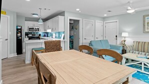 Une cuisine moderne avec des meubles blancs, une table à manger et des chaises. On y trouve également un coin salon avec un canapé et une lampe.
