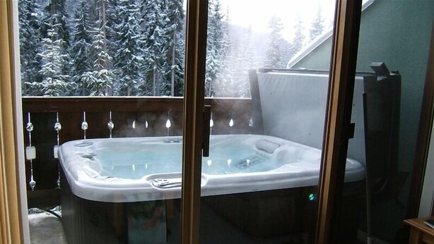 Een bubbelbad in een glazen balkon met uitzicht op een besneeuwd bos.